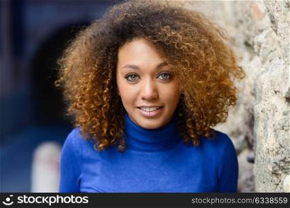 Close-up portrait of beautiful young African American woman with afro hairstyle and green eyes wearing blue sweater. Girl smiling.
