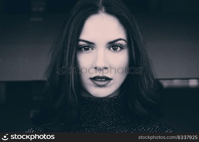 Close-up portrait of beautiful young woman looking at camera with intense look. Black and white and tinted photograph.