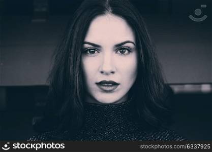 Close-up portrait of beautiful young woman looking at camera with intense look. Black and white and tinted photograph.