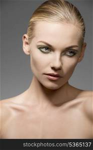 close-up portrait of caucasian female with blonde hair and beauty skin posing with pretty green make-up and naked shoulders