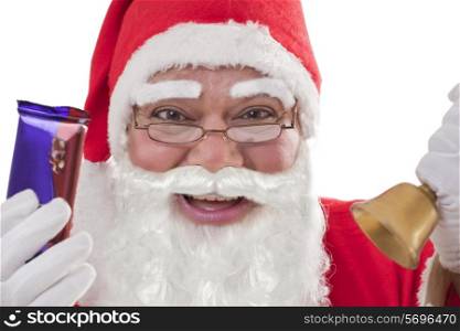 Close-up portrait of cheerful Santa Claus showing chocolates with bell and glasses