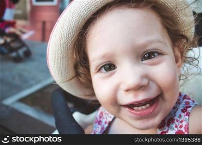 Close-up portrait of cute baby girl looking at camera smiling and wearing a hat