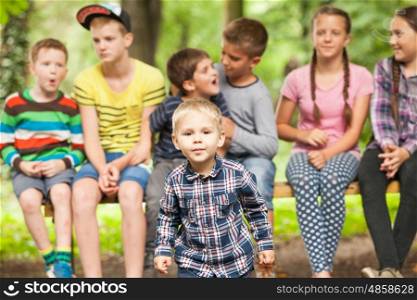 Close-up portrait of cute little boy in the foreground and a group of children on a bench behind him. Group of children outdoors
