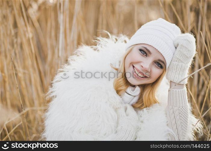 Close-up portrait of girl in white furry jacket and hat in the winter among the reeds.. Beautiful blond stands in winter in the reedbeds 9149.