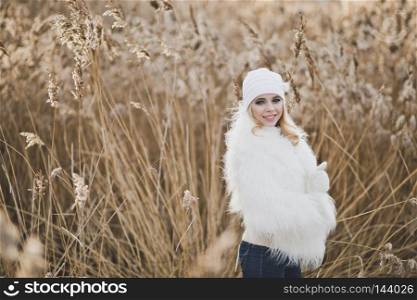 Close-up portrait of girl in white furry jacket and hat in the winter among the reeds.. Beautiful blond stands in winter in the reedbeds 9150.