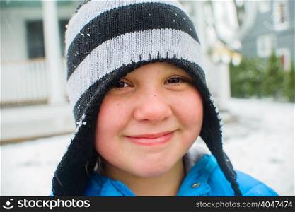 Close up portrait of girl wearing black and white striped hat in snowy garden