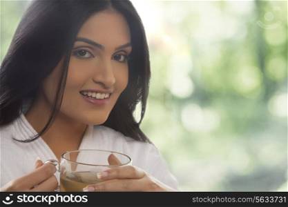Close-up portrait of happy young woman in bathrobe drinking tea