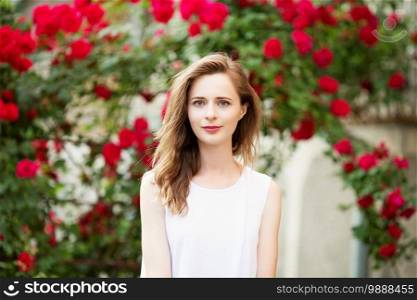 Close up portrait of lovely urban girl outdoors. Portrait of a happy smiling woman among the roses.