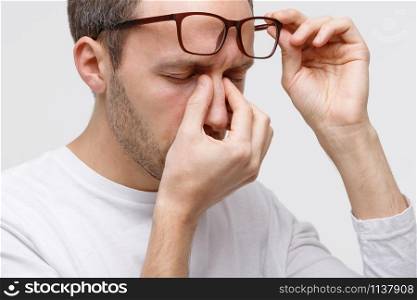 Close up portrait of man in eyeglasses rubbing his eyes and nose bridge, feels tired after working on laptop, isolated on white background. Overwork, exhausted, chronic fatigue, lack of sleep concept