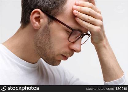 Close up portrait of man in glasses in white top touching his forehead, feels tired after working on laptop, white background. Overwork, exhausted, chronic fatigue, mental stress, headache concept.