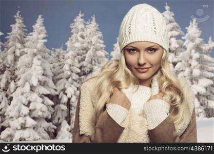 close-up portrait of pretty blonde girl in winter season, she posing with wool white hat, sweater and warm coat, smiling and looking in camera