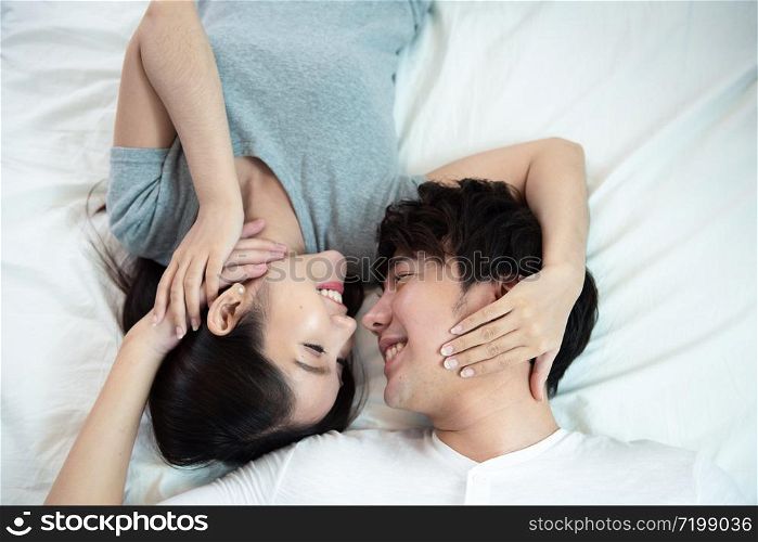 close up portrait of pretty young asian couple with happiness. asia man and woman lay on bed facing together with big smile hand touch face,love emotion with valentine concept .