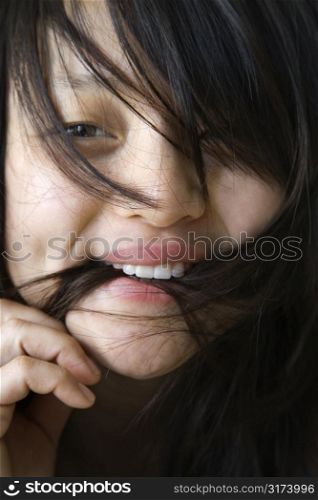Close up portrait of pretty young Asian woman biting her hair.
