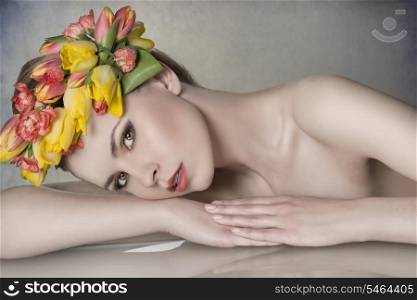 close-up portrait of sexy blonde girl with spring look posing lying on table with naked shoulders, colorful make-up and floral garland