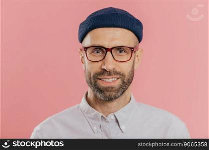 Close up portrait of smiling unshaven male, rejoices good news, wears hat and shirt, looks with eyes full of joy isolated over pink background. European man with bristle ready for date with girlfriend