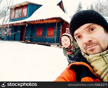 Close up portrait of smiling young couple having fun outdoors. Man and woman enjoying themselves on a winter day. Traditional mountain village wooden house in the background