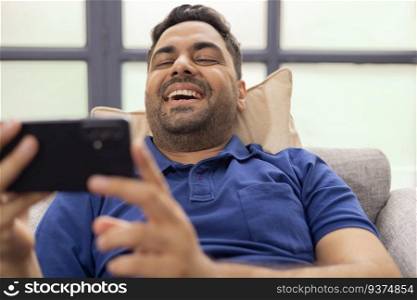 Close-up portrait of smiling young man using  Mobile Phone while sitting on sofa at home