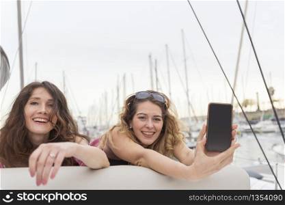 Close up portrait of Two excited girlfriends with mobile phones lying down and laughing and looking in camera.