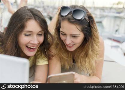 Close up portrait of Two excited girlfriends with mobile phones lying down and laughing and looking in camera.