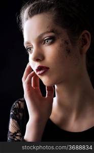 close up portrait of very beautiful young lady actrees over a dark background with dirty make up and fashion light, she is turned of three quarters at right, she looks in front of her and her right hand is near the face