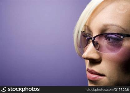 Close-up portrait of young adult Caucasian blond woman on purple background wearing sunglasses.