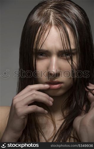 close-up portrait of young girl with clean skin, long wet hair and some water drops on the face. Looking in camera with angry expression
