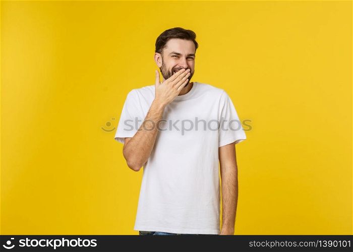 Close up portrait of young man laughing with hand covering mouth by yellow background.. Close up portrait of young man laughing with hand covering mouth by yellow background