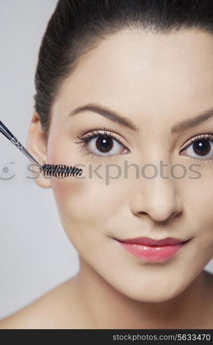 Close-up portrait of young woman applying mascara