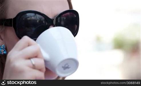 Close up portrait of young woman in sunglasses drinking coffee in the street cafe