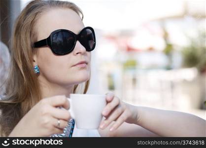 Close up portrait of young woman in sunglasses drinking coffee in the street cafe