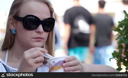 Close up portrait of young woman in sunglasses eating ice cream in the street cafe