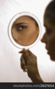 Close up portrait of young woman looking in handheld mirror