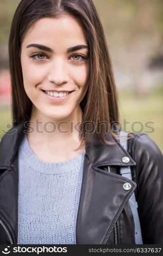 Close-up portrait of young woman smiling in urban background wearing casual clothes. Girl wearing striped sweater and leather jacket