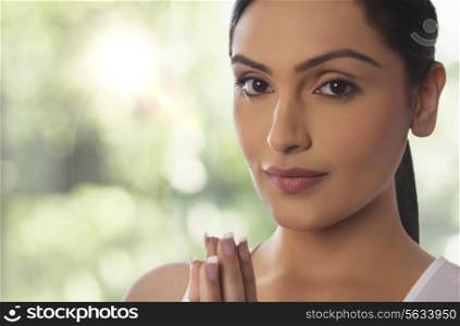 Close-up portrait of young woman with hands clasped against glass window