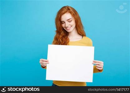 Close up Portrait young beautiful attractive ginger red hair girl smiling showing blank sign. Blue Pastel Background. Copy space.