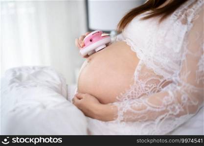 close-up pregnant woman listening to fetal heart sound through headphones on a bed