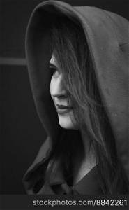 Close up pretty young woman wearing coat with hood monochrome portrait picture. Closeup side view photography with grey background. High quality photo for ads, travel blog, magazine, article. Close up pretty young woman wearing coat with hood monochrome portrait picture