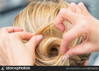 Close up rear view of hairdresser making hairstyle for long hair of blonde woman.. Hairstylist making bride wedding hairstyle