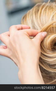 Close up rear view of hairdresser making hairstyle for long hair of blonde woman.. Hairstylist making bride wedding hairstyle