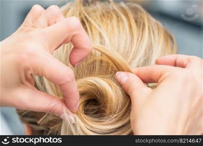 Close up rear view of hairdresser making hairstyle for long hair of blonde woman.. Hairstylist making bride wedding hairstyle