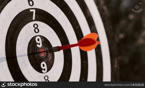 Close up red dart arrow hitting target centre dartboard on sunset background. Business targeting and focus concept.