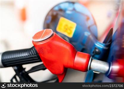 Close-up red fuel nozzle. Gasoline pump nozzle. Car fueling at gas station. Refuel fill up with petrol gasoline. Petrol pump filling fuel nozzle in fuel tank of car at gas station. Oil price crisis.
