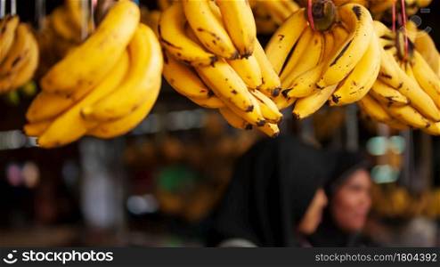 Close-up ripe bananas fruits display at a local grocery. Bunch of ripe yellow bananas fruits with dark spots display at a local grocery. Females vendor blurred in the background.