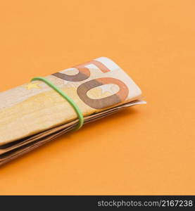 close up rolled up euro note tied with rubber orange backdrop