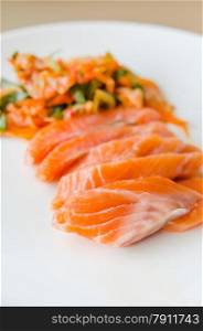 close up salmon sashimi with kimchi on white dish . Salmon sashimi