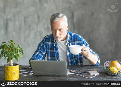 close up senior man holding coffee cup using laptop charged with power bank