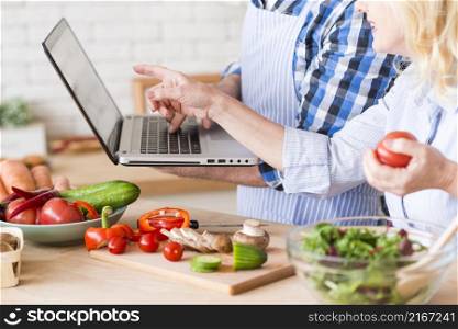 close up senior woman pointing laptop hold by her husband while preparing vegetable salad