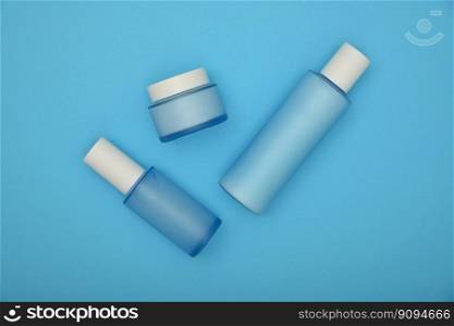 Close up set of three cosmetic skin care cream, lotion and tonic bottles over pastel blue background, elevated top view, directly above