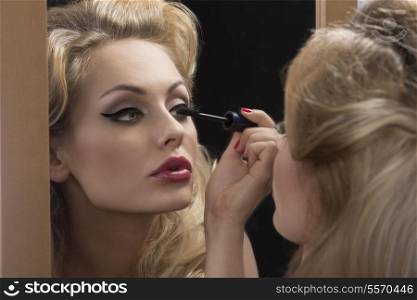 close-up shoot of fashion elegant woman applying mascara in front of the mirror, blonde hair-style