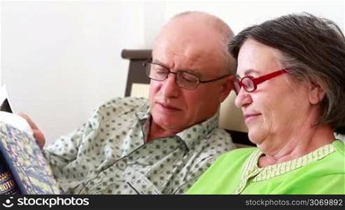Close up shot of a a loving senior couple watching a photo album full of memories, while lying in bed in the morning.